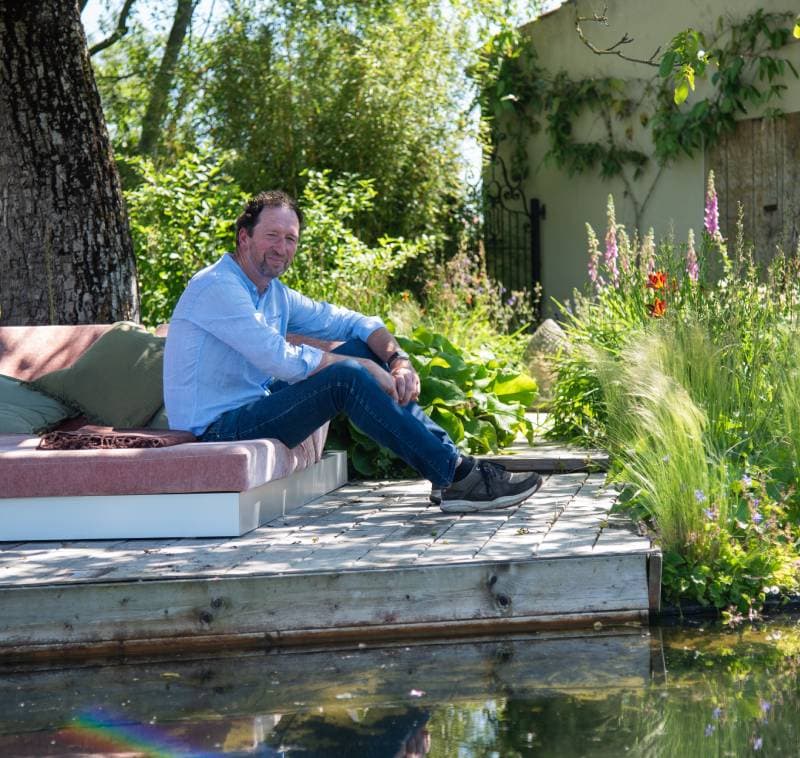 diensten_advies Man ontspant in een groene tuin met water en bloemen, eco-vriendelijk tuinontwerp.