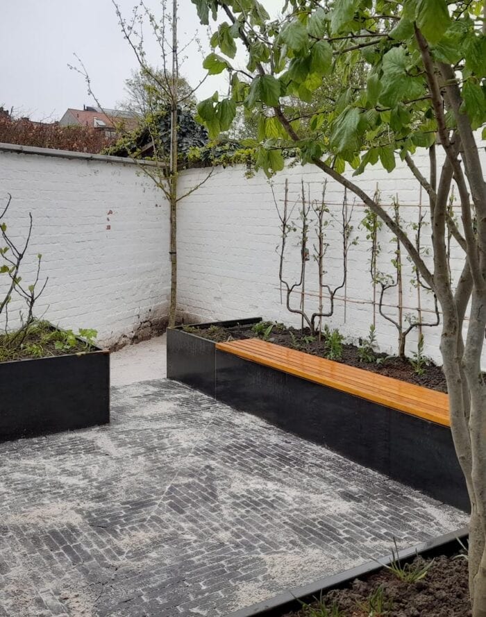 Moderne tuin met verhoogde plantenbakken en houten bank in een groene omgeving.